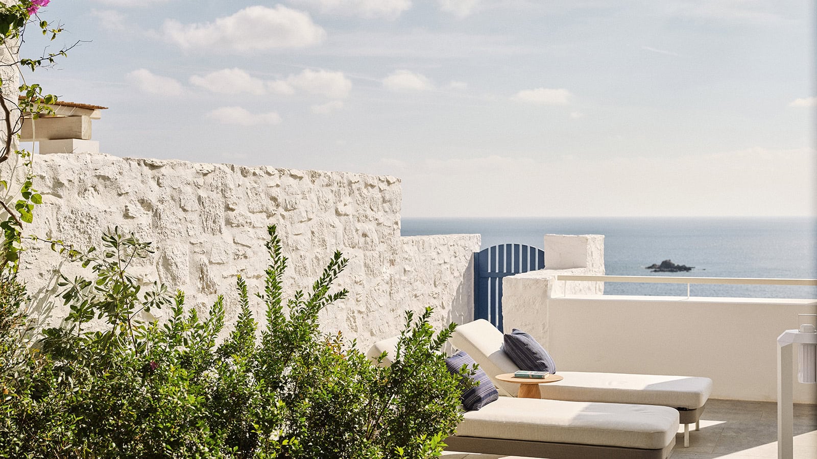 Terrasse mit Sonnenliegen und weiß gekalkter Mauer im Four Seasons Mykonos, dahinter das Meer.