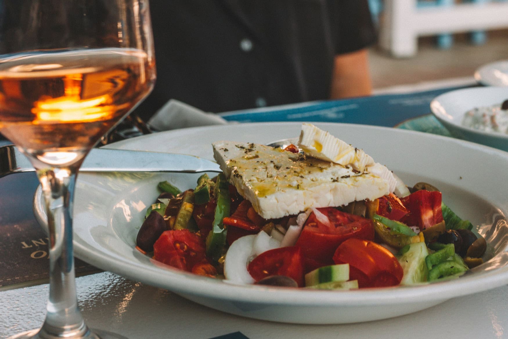 Griechischer Bauernsalat mit Feta, Tomaten, Gurke und Oliven neben einem Glas Rosé am Tavernentisch