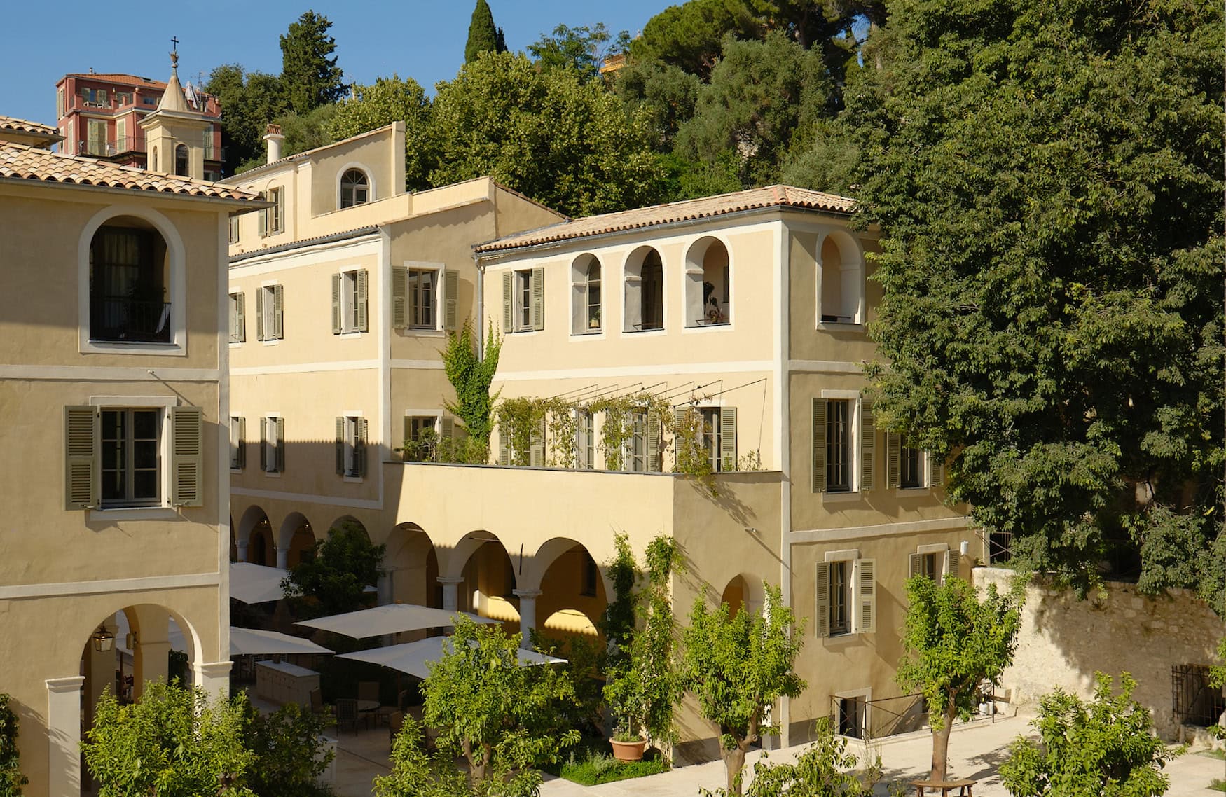 Innenhof des Hôtel du Couvent in Nizza mit Arkaden, grünen Fensterläden und mediterranem Baumbestand.