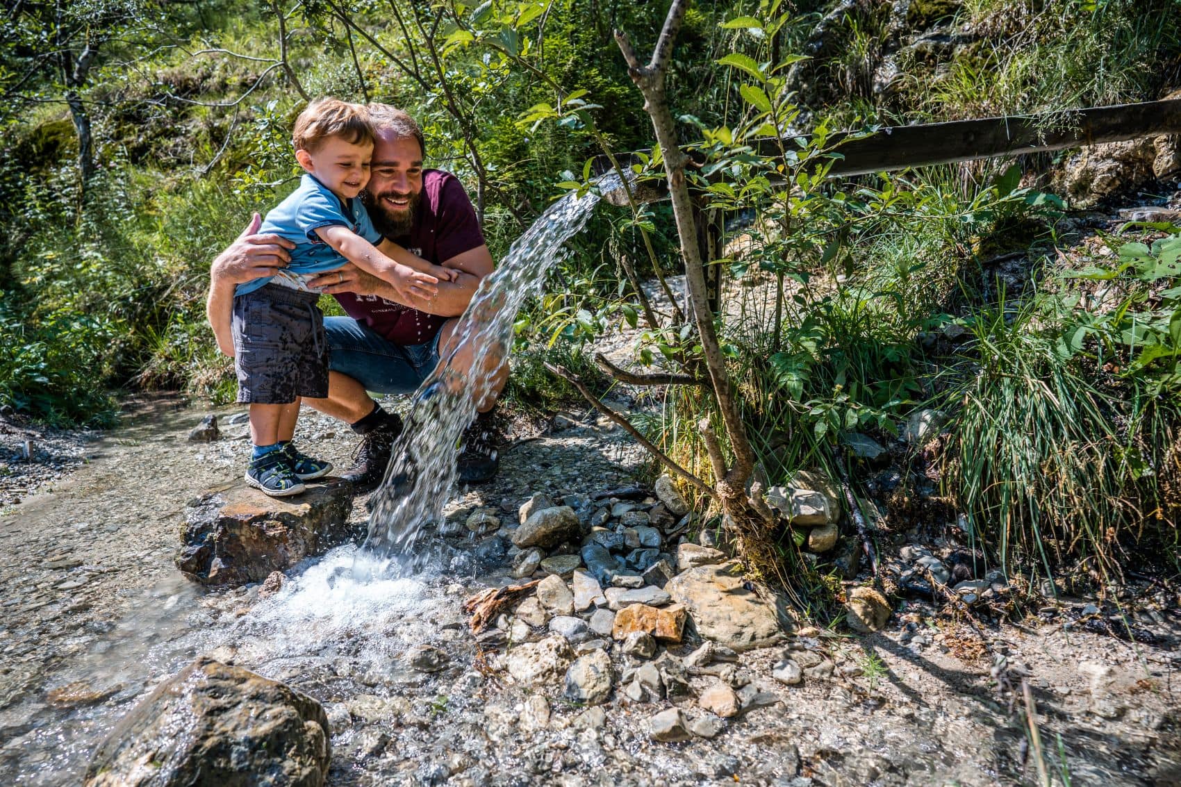 Vater und Kind kühlen sich an einer Quelle im Jenbachtal bei Bad Feilnbach im Chiemsee-Alpenland ab.