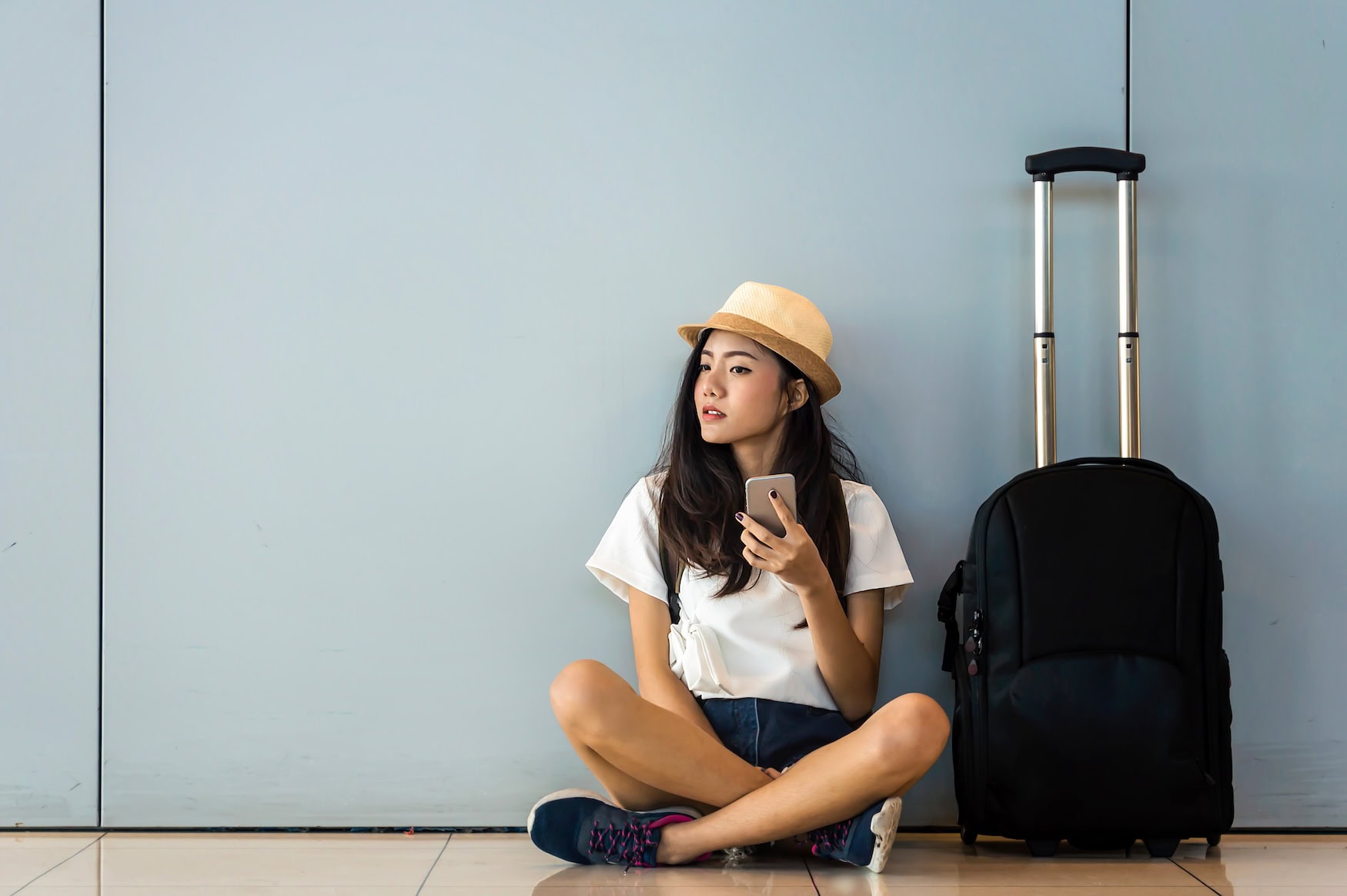 Eine junge Frau lehnt im Flughafen an einer Wand.