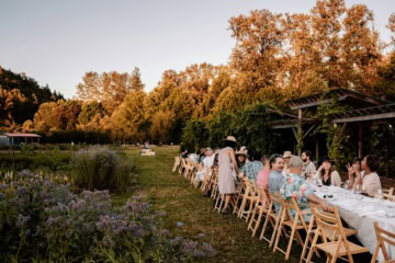 Lange festlich gedeckte Tafel im Freien bei Abendlicht, viele Gäste feiern an einem Sommerabend