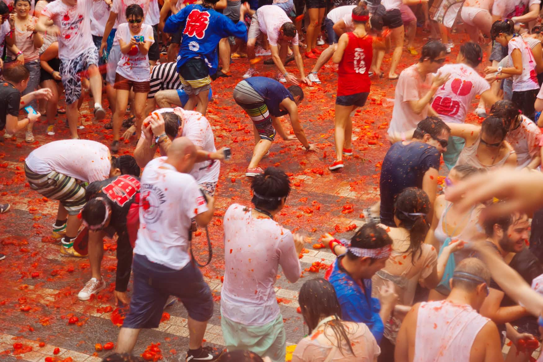 Menge feiernder Menschen in einer mit zermatschten Tomaten bedeckten Gasse bei der Tomatina in Buñol