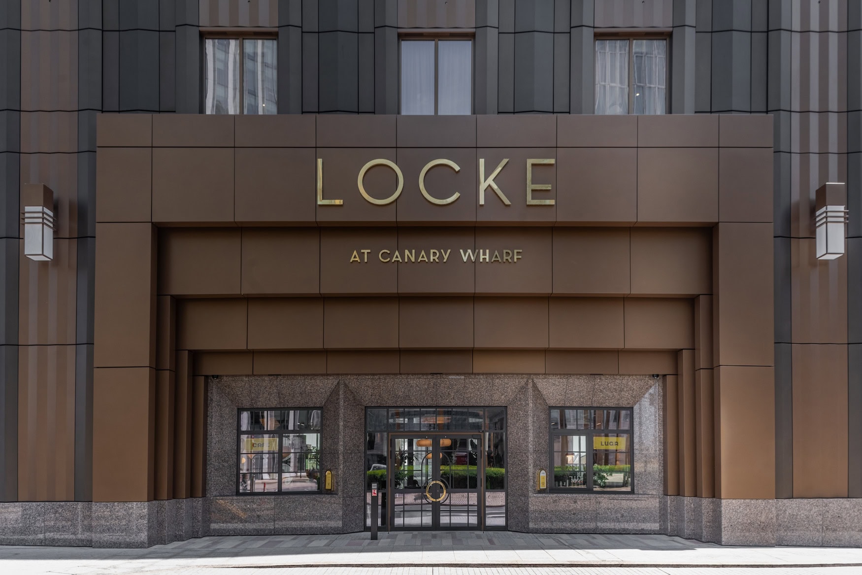 Eingang des Locke at Canary Wharf mit bronzefarbener Fassade und goldenem Schriftzug