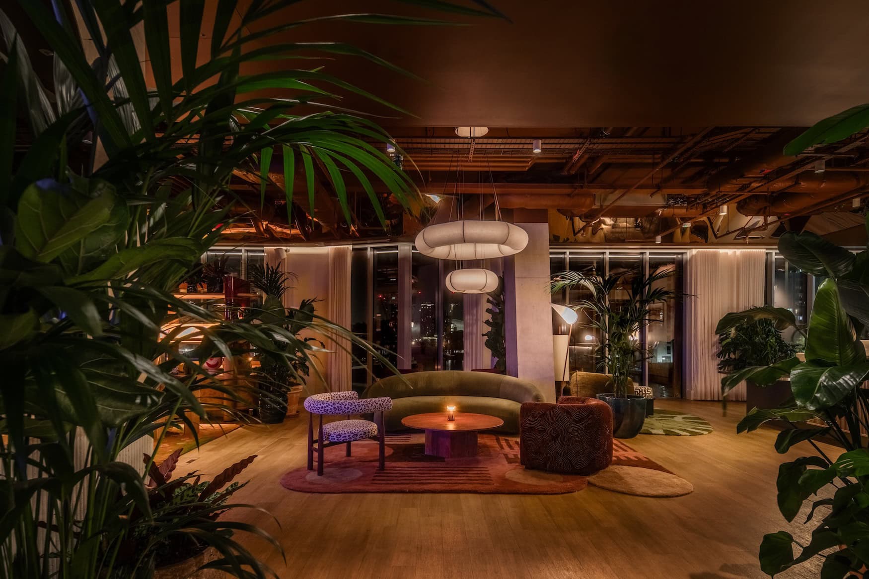 Begrünte Lounge im Locke Canary Wharfmit geschwungenem Sofa und warmem Licht am Abend