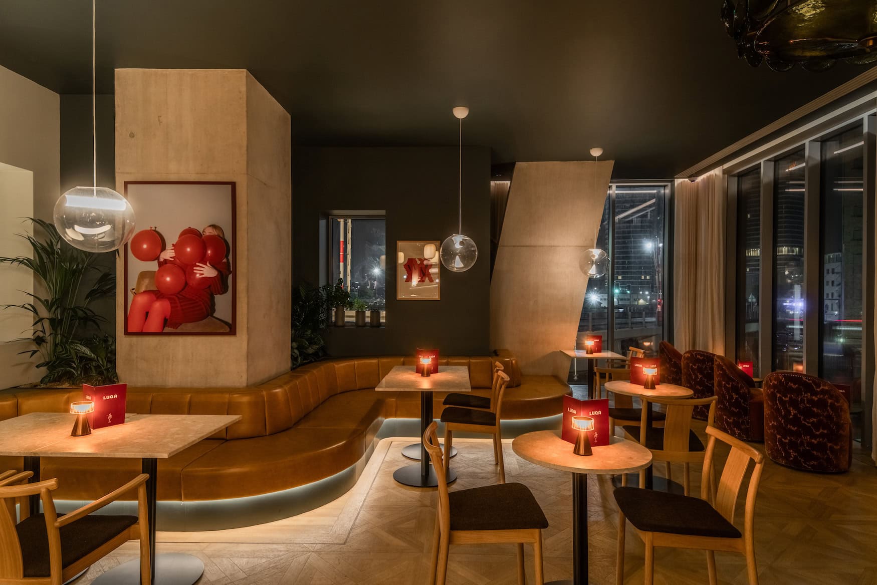 Café-Restaurant Luqa im Locke Canary Wharf mit Lederbank, Kunst an der Wand und Kugelleuchten bei Abendlicht