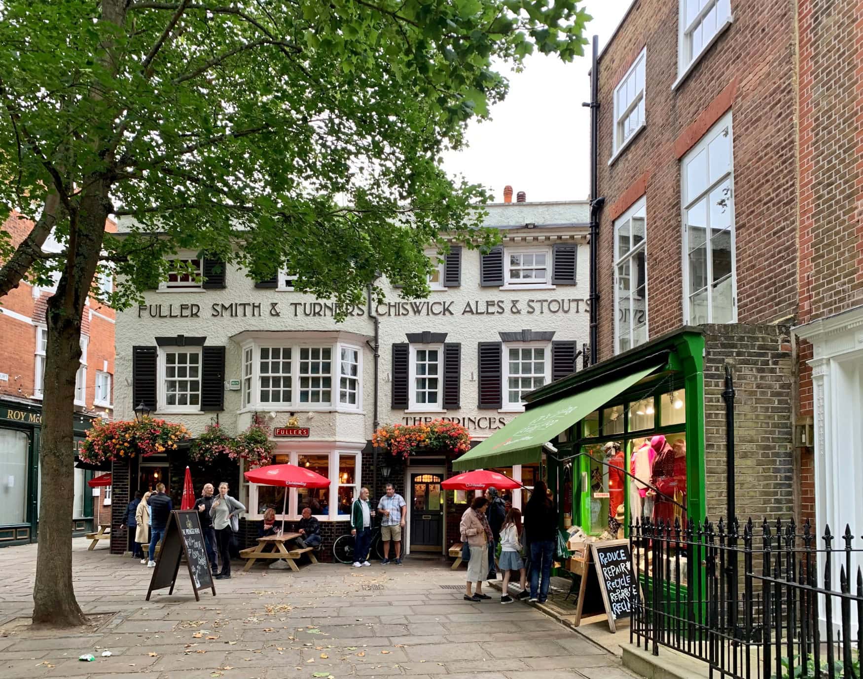 Fassade des Pubs The Princes Head in Richmond, London, davor einige Bänke mit roten Sonnenschirmen.