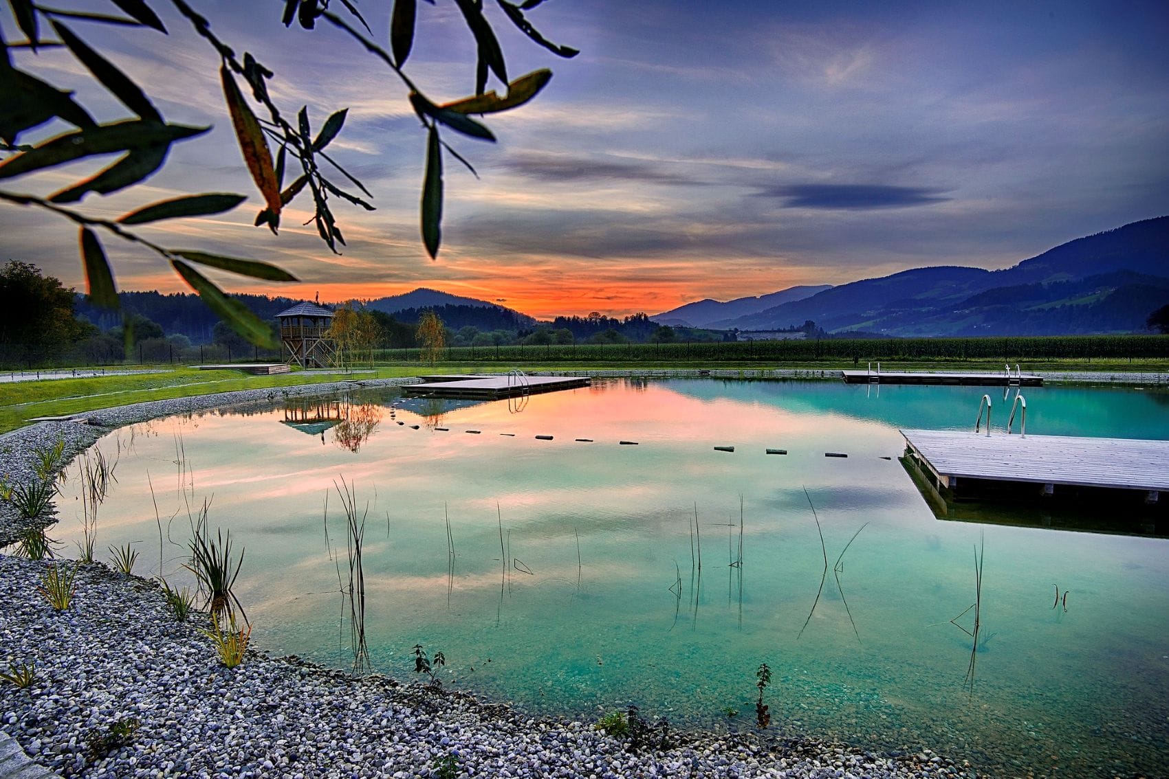 Das Naturbad Radlje ob Dravi in Slowenien mit klarem Wasser und Holzstegen bei Sonnenuntergang.