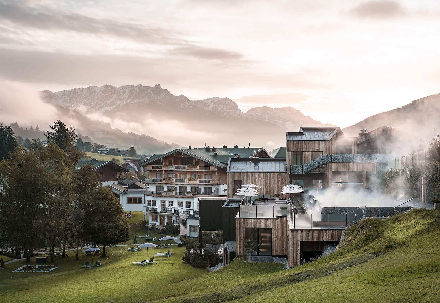 Herbstliche Außenansicht des Naturhotel Forsthofgut in Leogang mit Holzarchitektur, Pool und Bergkulisse.