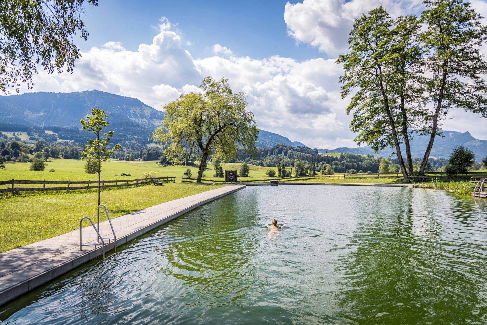 Naturschwimmbad Samerberg im Chiemsee-Alpenland mit Badenden vor der Kulisse der Bayerischen Alpen.