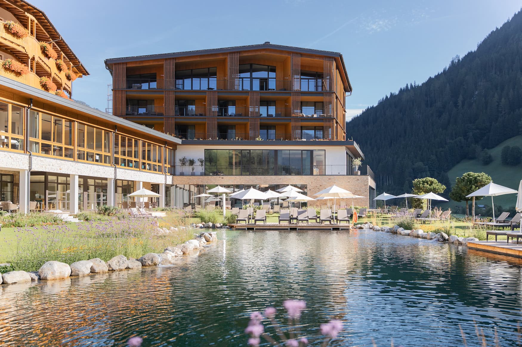 Sommerliche Ansicht des Hotel Nesslerhof in Großarl mit Naturschwimmteich, Sonnenschirmen und Bergkulisse.