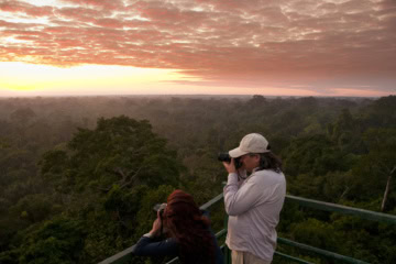 Sonnenaufgang über dem Regenwald im Tambopata-Nationalreservat mit zwei Personen auf einem Aussichtsturm