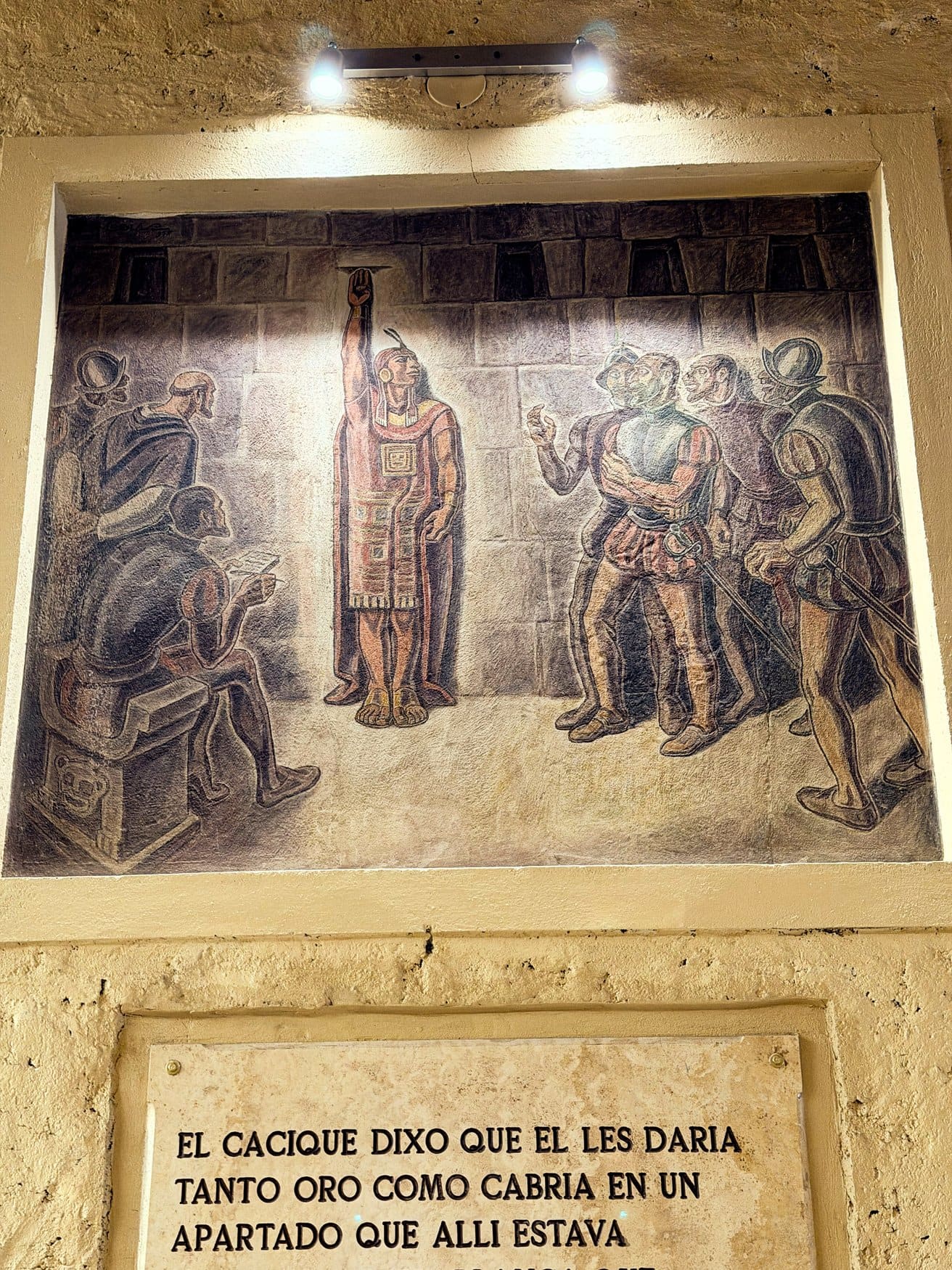 Wandbild in einer Nische, das den Inka Atahualpa mit erhobener Hand vor spanischen Konquistadoren zeigt. Darunter ist eine Tafel mit einer historischen Inschrift in spanischer Sprache angebracht.