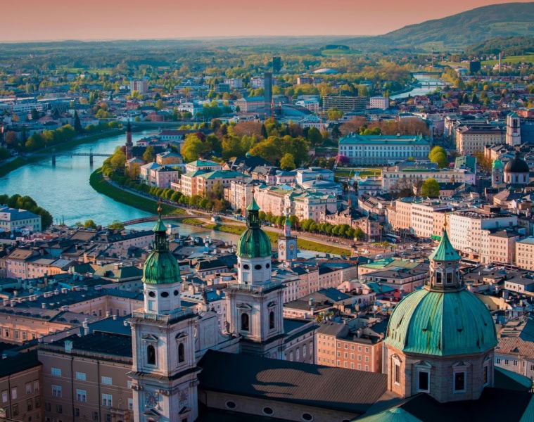 Luftaufnahme der Stadt Salzburg in Österreich im Abendlicht, mittig von der Salzach durchkreuzt