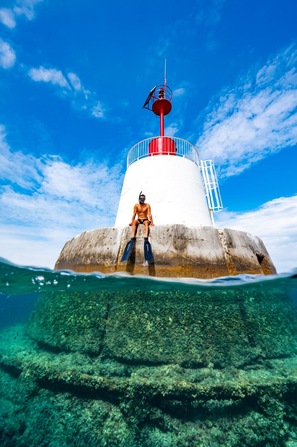 Schnorchler mit Flossen sitzt an einem Leuchtturm vor Istrien, während unter der Wasseroberfläche der felsige Meeresgrund zu sehen ist