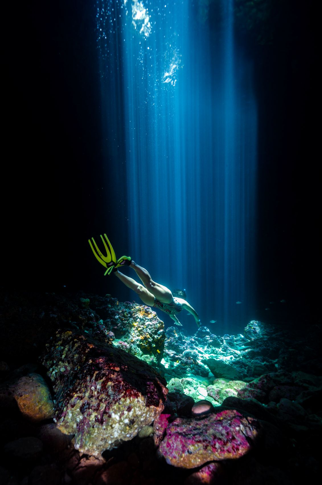 Schnorchler taucht durch eine dunkle Unterwasserhöhle vor Istrien, in die Sonnenstrahlen von der Wasseroberfläche fallen