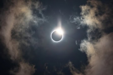 Die Sonne an einem blauen Himmel mit einigen Wolken wird fast vollständig vom Mond verdeckt.