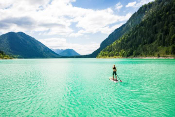 Stand-up-Paddlerin auf dem türkisfarbenen Sylvensteinsee bei Lenggries vor der Kulisse der Bayerischen Alpen.