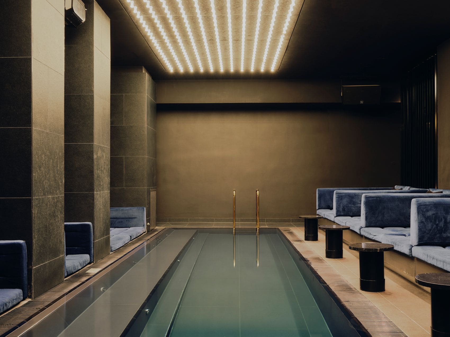 Innenpool im Wellnessbereich des The Dean Munich mit eleganten Liegen, dunklem Design und stimmungsvoller Deckenbeleuchtung.