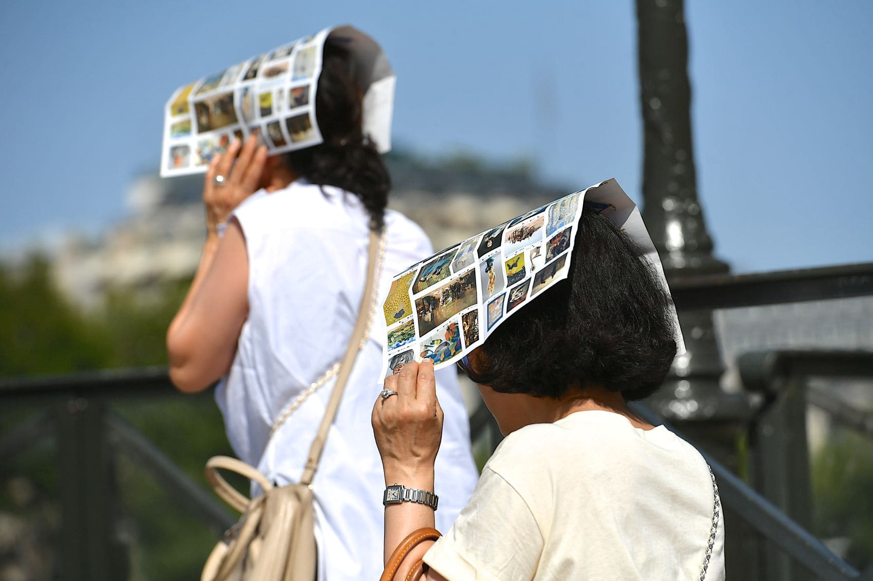 Zwei Touristinnen schützen sich in Paris mit Prospekten vor der intensiven Sommersonne.