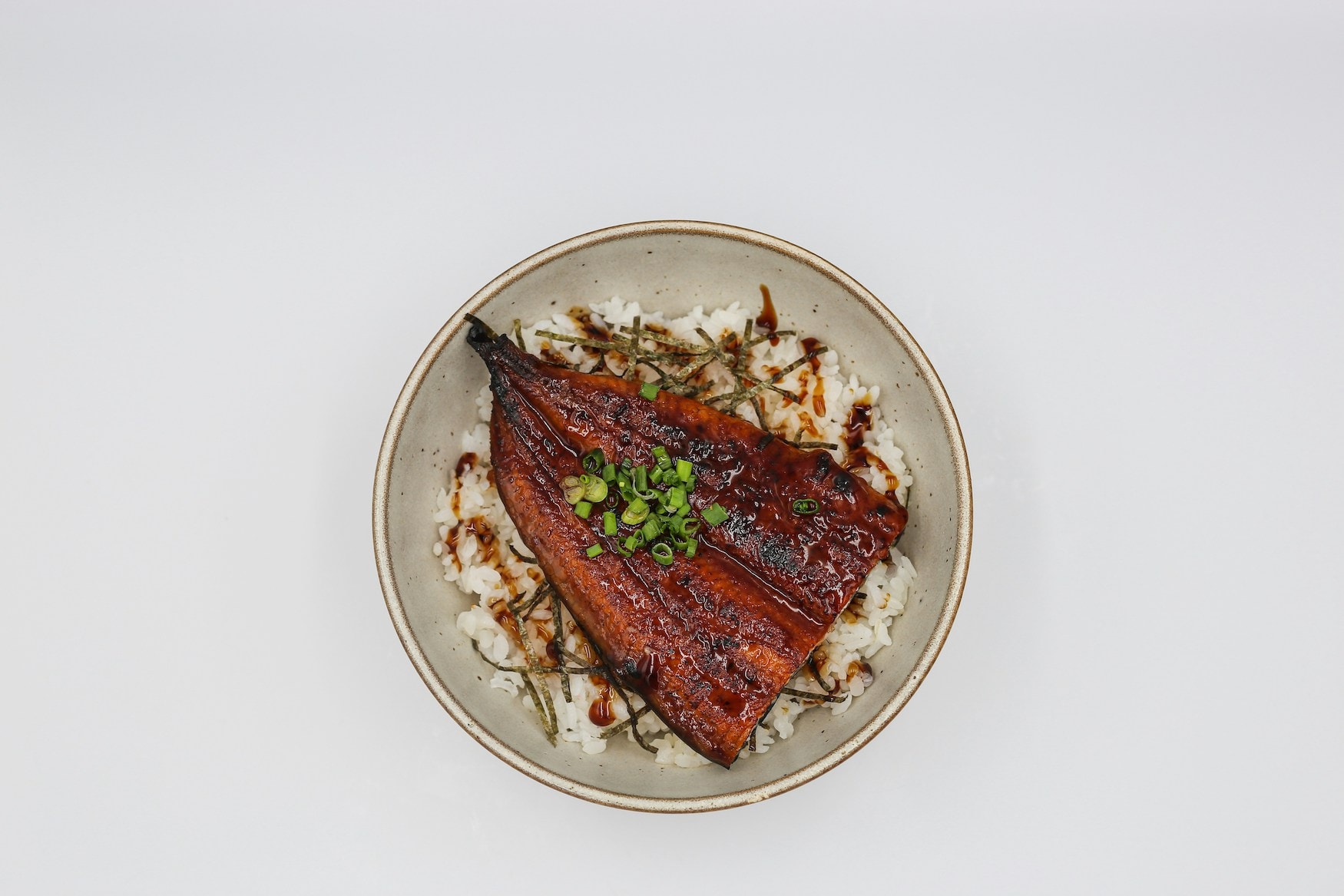 Gegrilltes Unagi-Filet mit glänzender Glasur auf Reis in einer Keramikschale, von oben