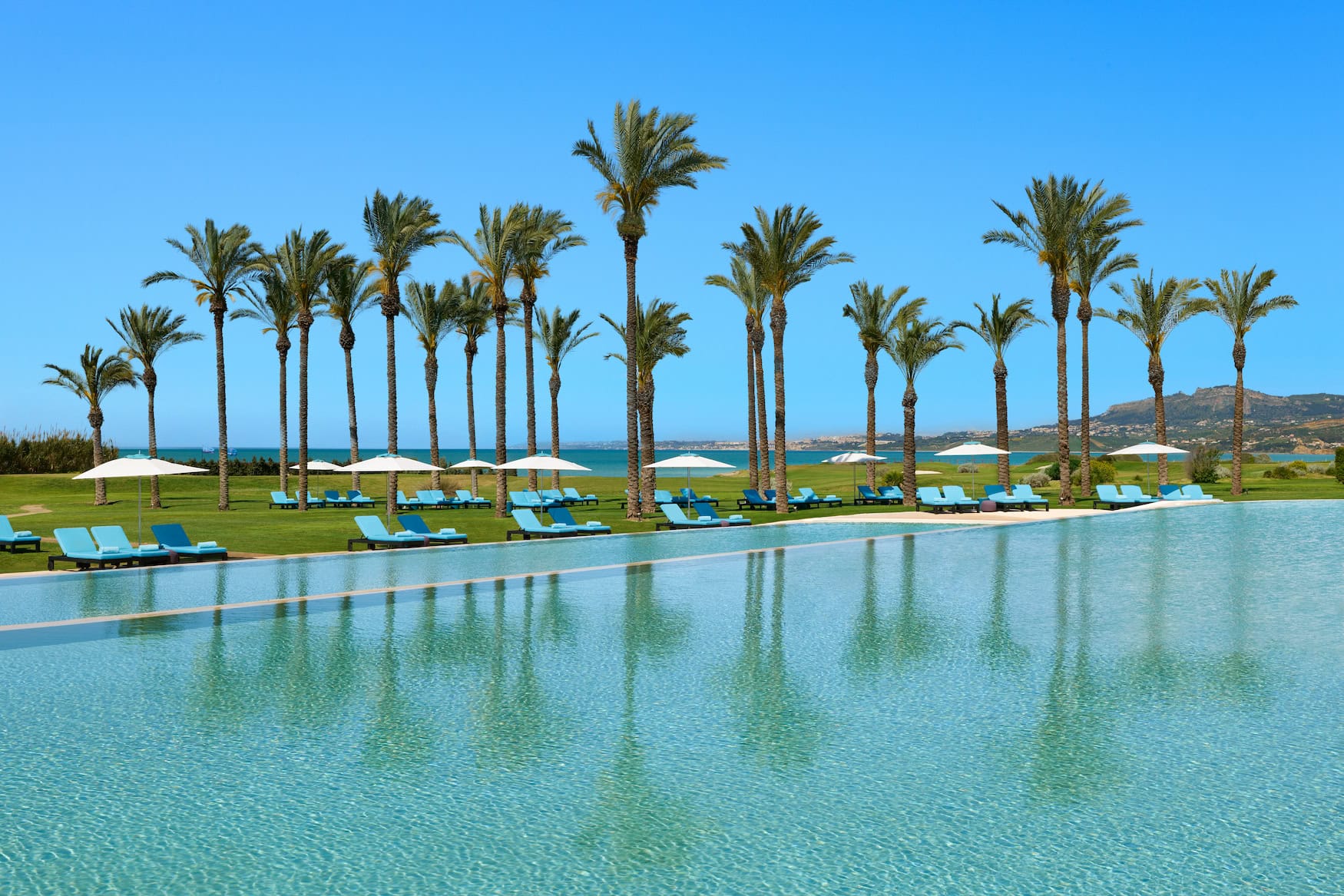 Poollandschaft des Verdura Resort an der Südküste Siziliens mit Palmenreihe und Blick aufs Mittelmeer.