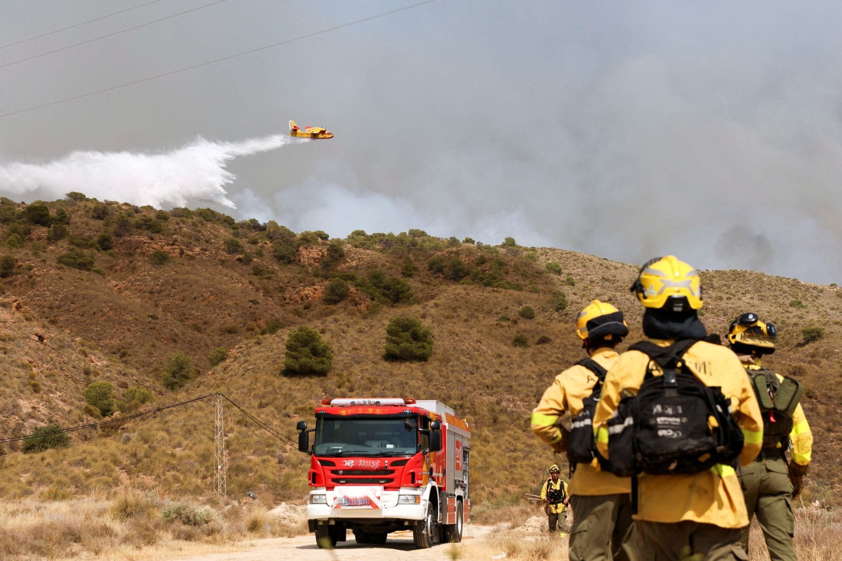 Ein Löschflugzeug wirft Wasser über einem Waldbrand bei Los Gallardos in der spanischen Provinz Almería ab, während Einsatzkräfte den Brand am Boden bekämpfen.