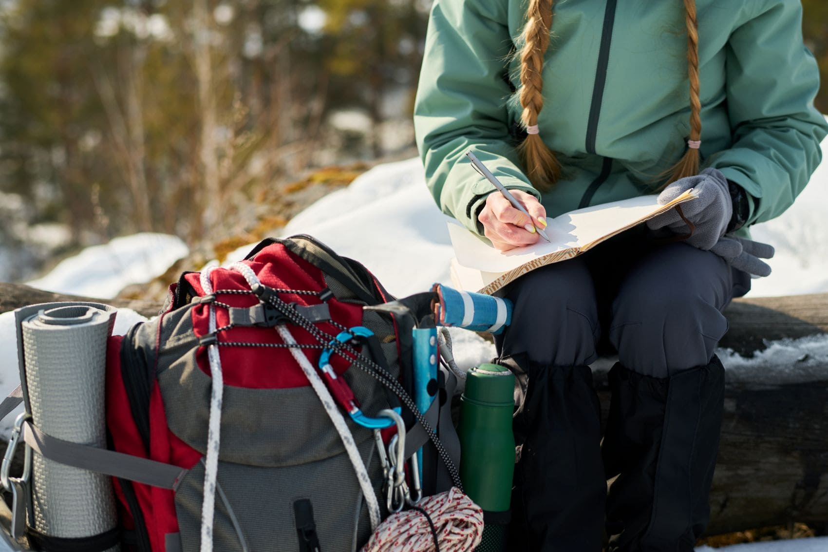 Ein gepackter Wanderrucksack mit Trinkflasche und Isomatte liegt neben einer Wanderin, die ihre Tour plant.