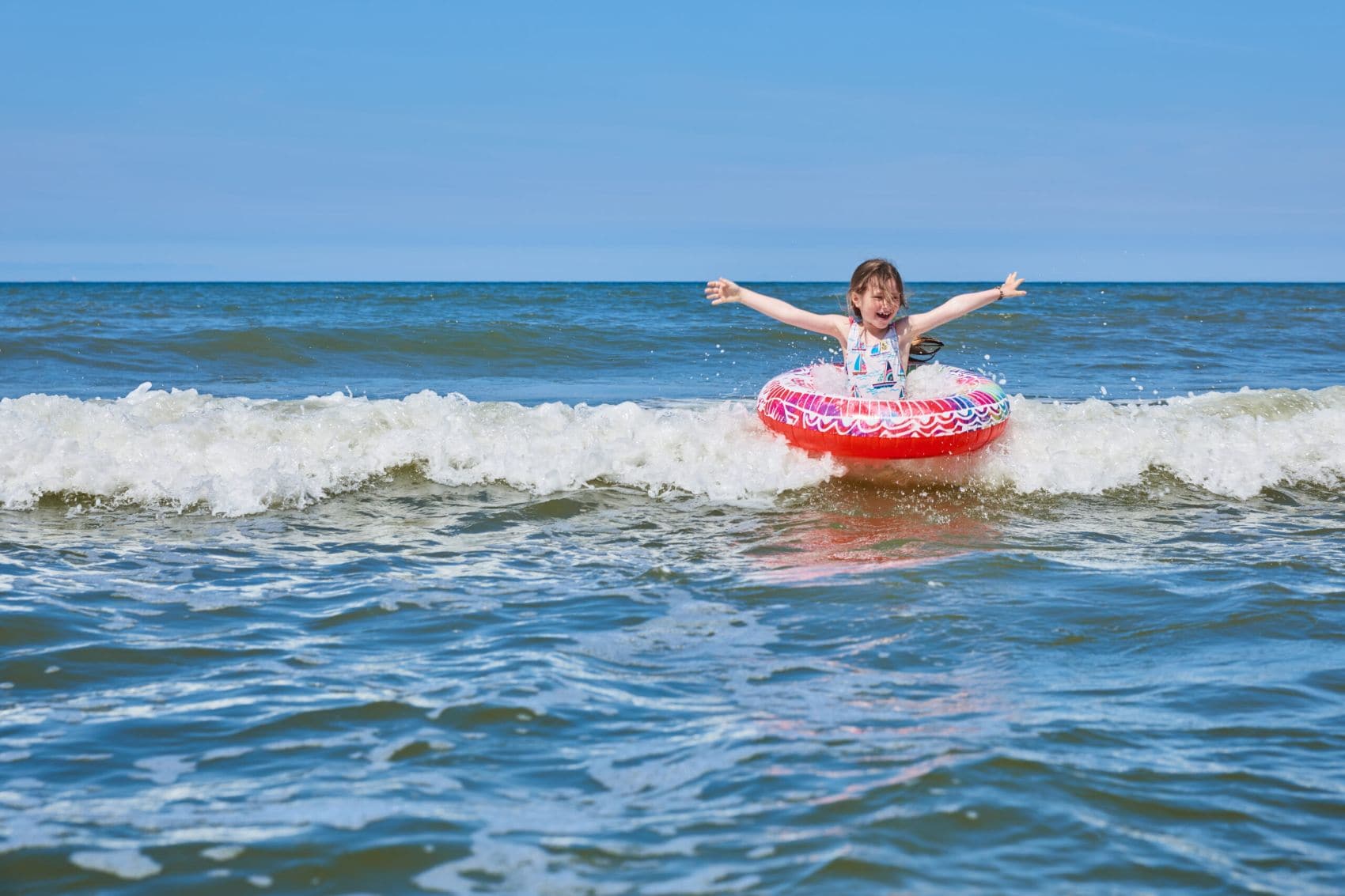 Ein Kind spielt mit einem Schwimmring in den Wellen der Nordsee am Strand von Wangerooge.