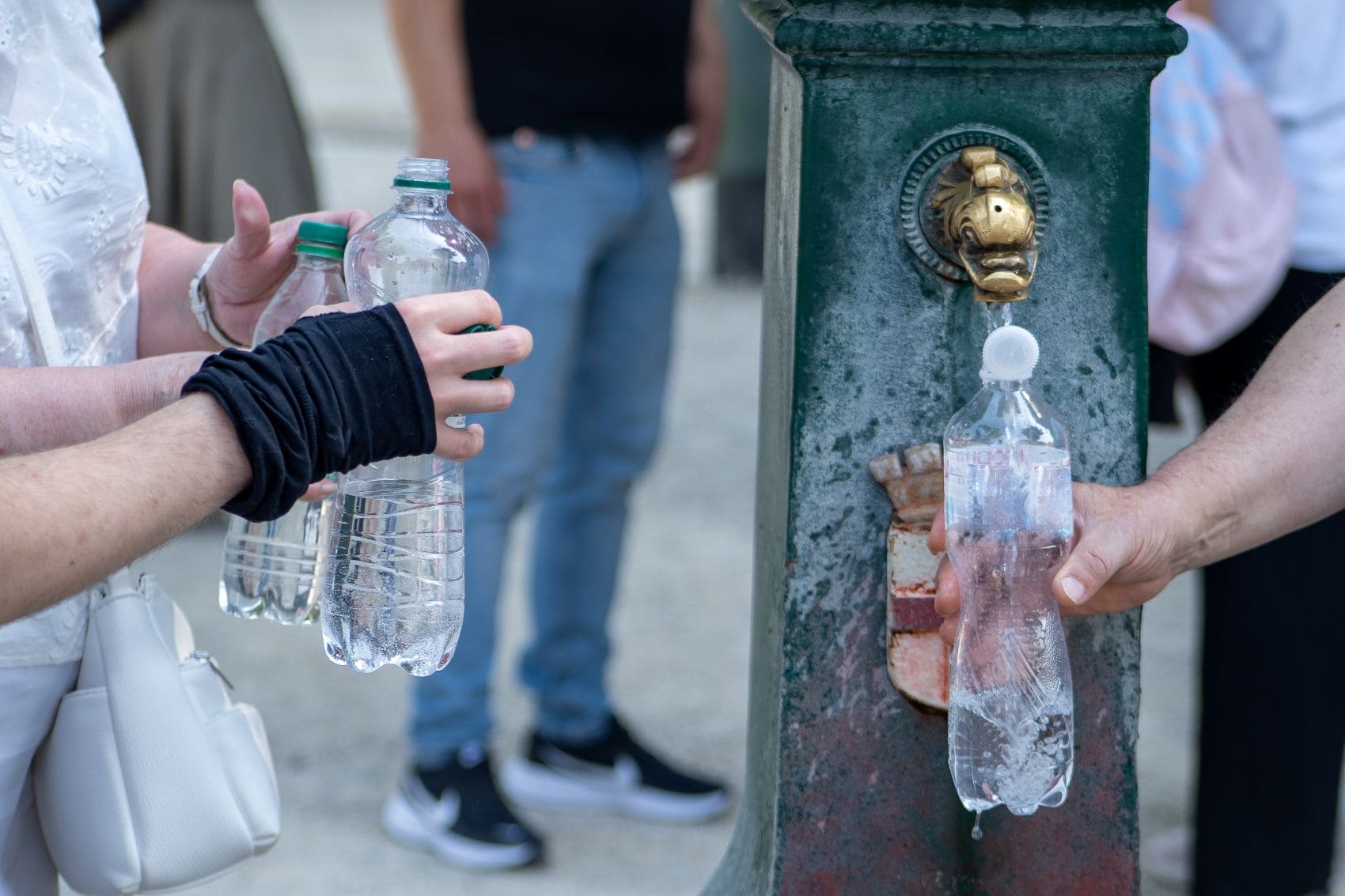 Reisende füllen an einem öffentlichen Trinkbrunnen Wasserflaschen auf, um sich während einer Hitzewelle mit ausreichend Flüssigkeit zu versorgen.