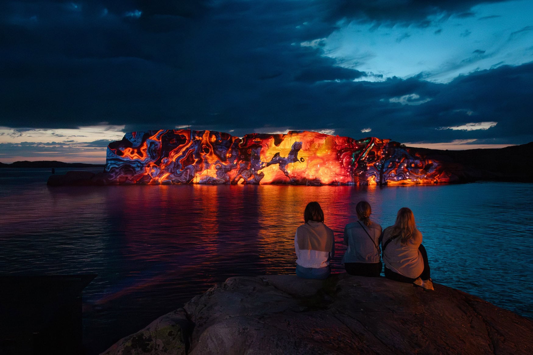Beleuchtete Felswand am Wasser beim Island of Light Festival in Smögen, davor Betrachter im Dunkeln