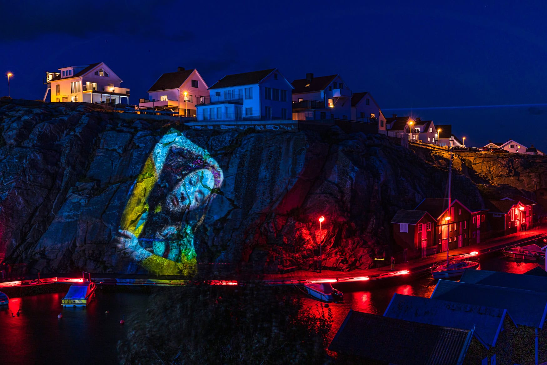 Lichtkunst-Projektion eines Porträts auf einer Felswand über dem Hafen von Smögen beim Island of Light Festival