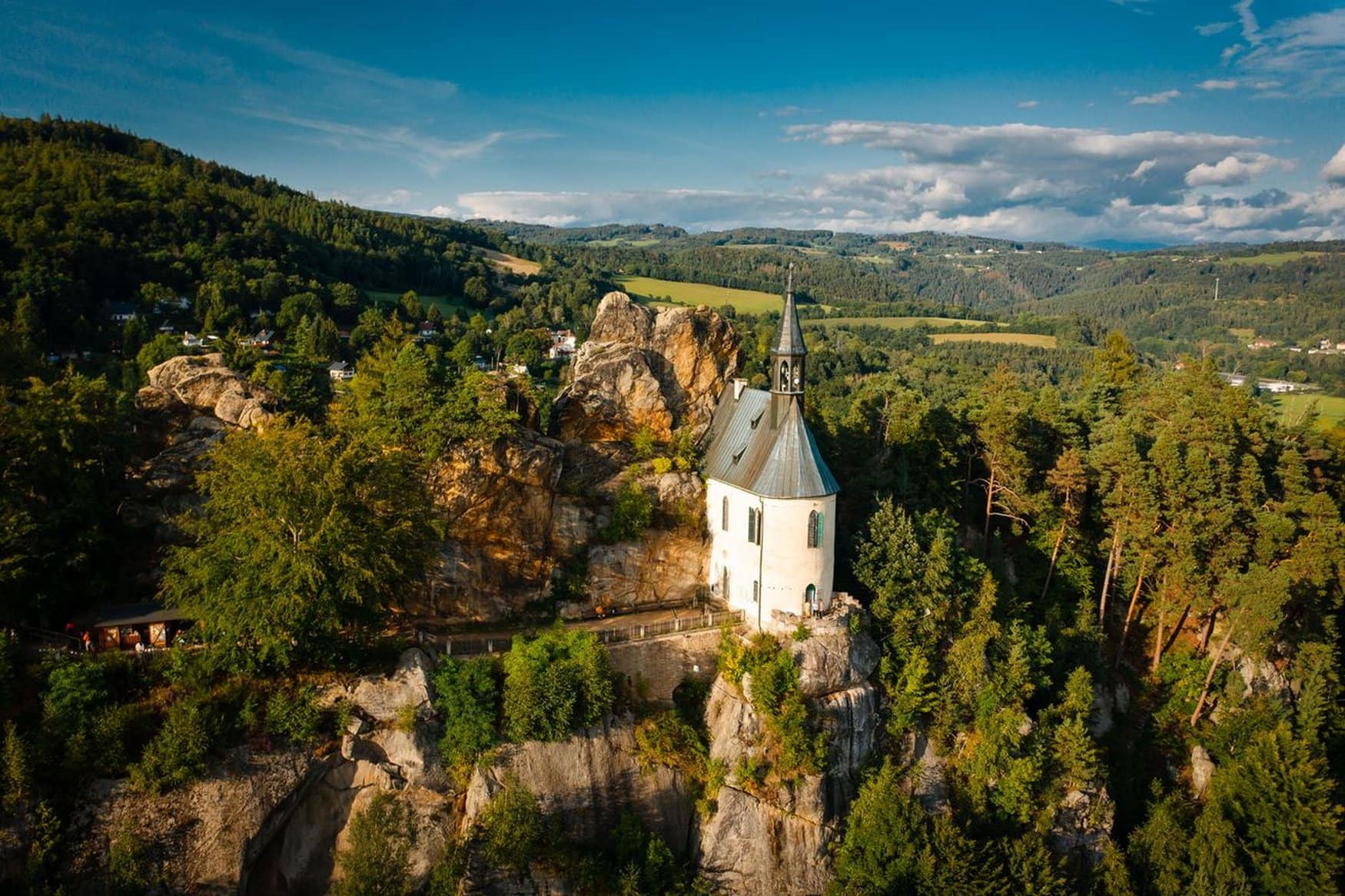Die kleine Kapelle Pantheon auf einem Felsen bei Burg Vranov im Böhmischen Paradies, umgeben von Wald und hügeligem Land unter blauem Himmel.