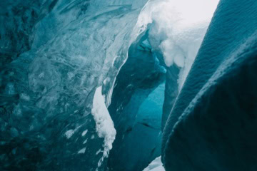 Blick aus einer Gletscherhöhle, geschliffenes blaues Eis wölbt sich über einem schneebedeckten Durchgang