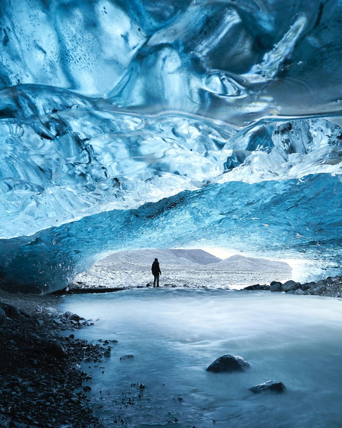 Silhouette einer Person am Ausgang einer Eishöhle, darüber die blau geschliffene Decke aus Gletschereis
