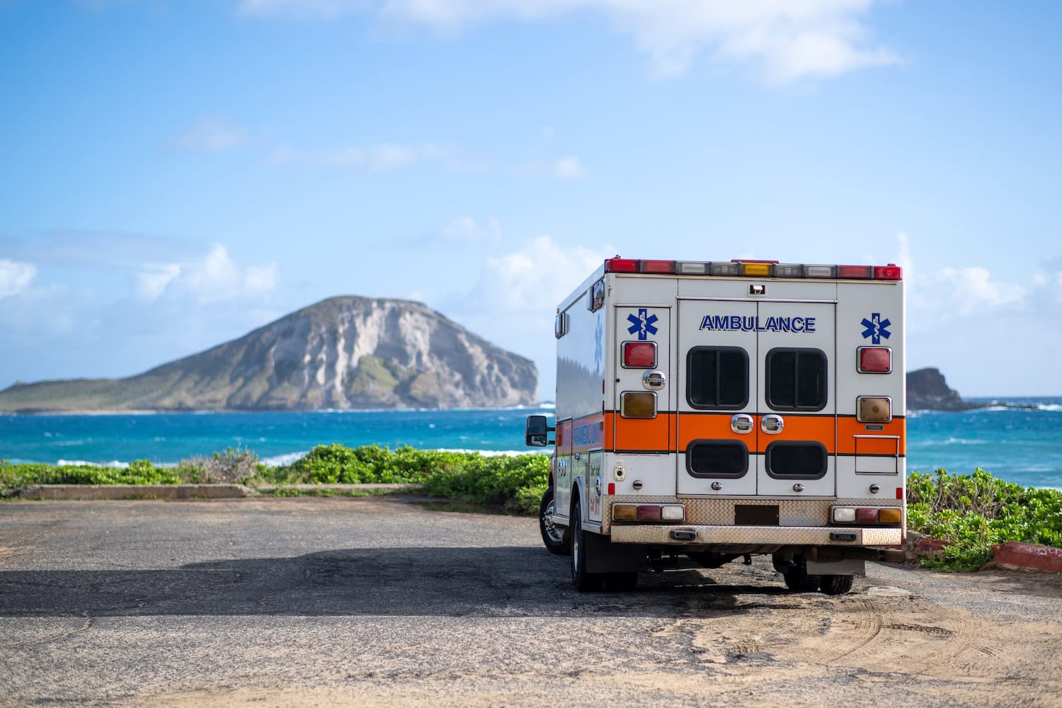 Ein Krankenwagen steht auf einem Parkplatz am Makapuu Beach Park, im Hintergrund eine weitere Insel mit Vulkan.