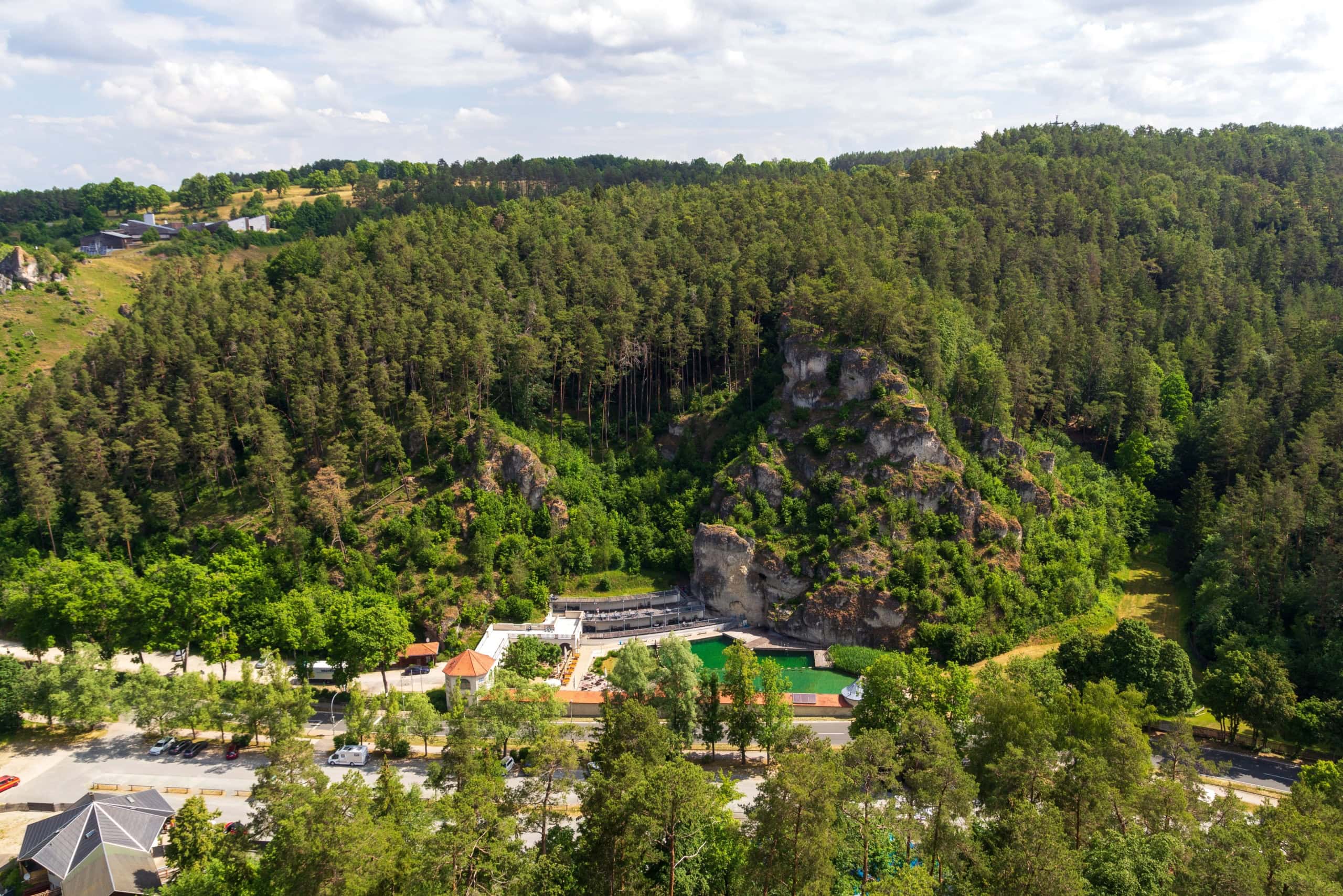 Luftaufnahme des Felsenbads Pottenstein in der Fränkischen Schweiz mit grünem Becken zwischen bewaldeten Felsen.