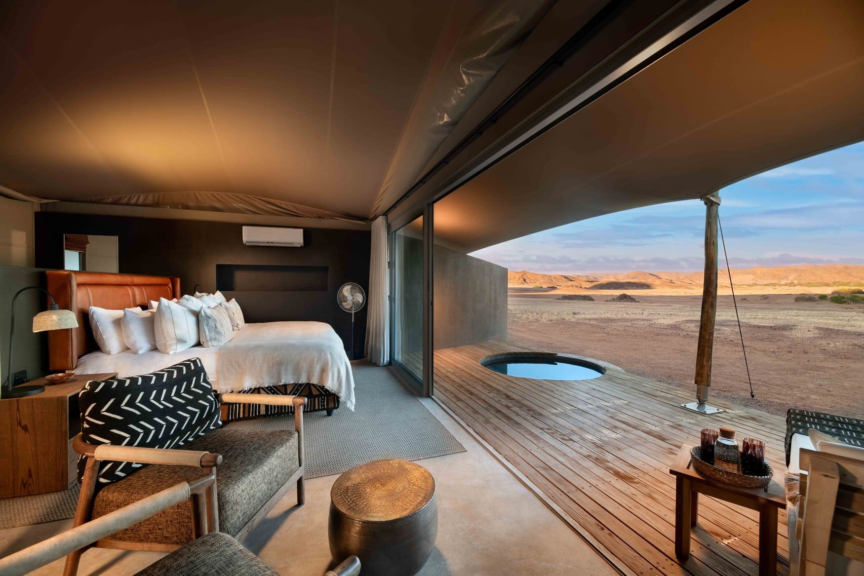 Schlafzimmer in einem Gastzelt mit Blick auf die Terrasse und einen runden Plunge-Pool in der Wüstenlandschaft.