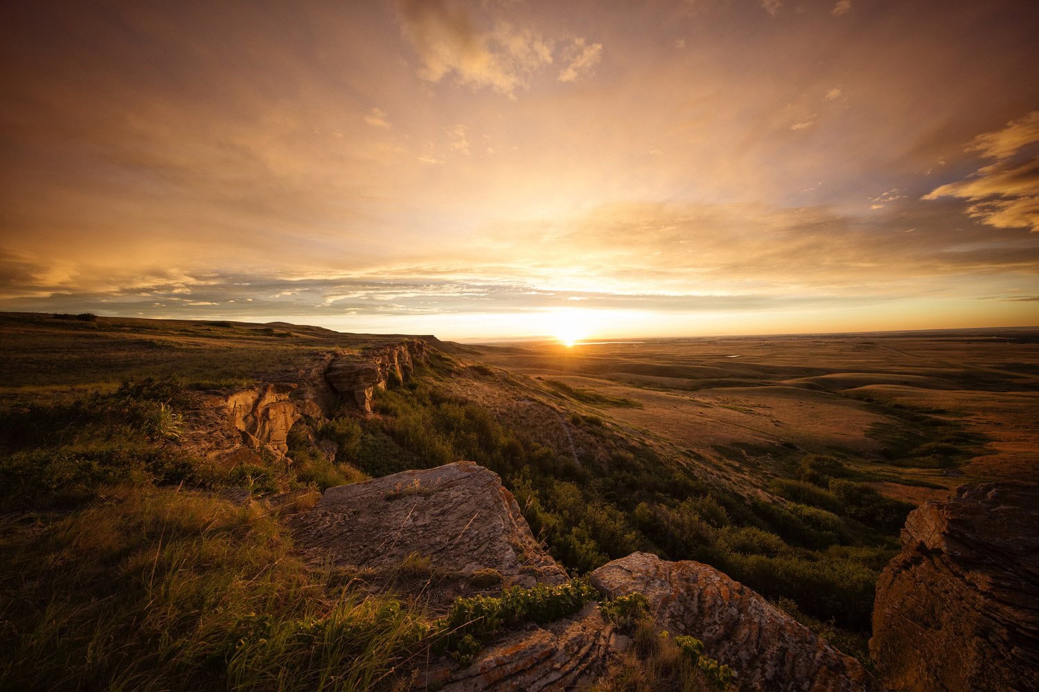 Sonnenuntergang über der Sandsteinklippe von Head-Smashed-In Buffalo Jump, im Hintergrund die weite Prärie Südalbertas in warmem Licht