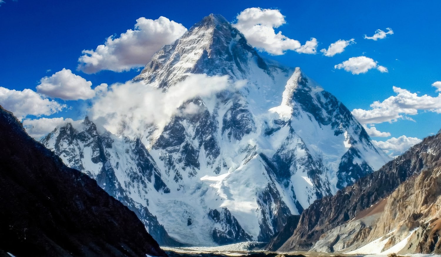 Die Gipfelpyramide des K2 ragt über schneebedeckte Flanken, Wolken ziehen um den Grat