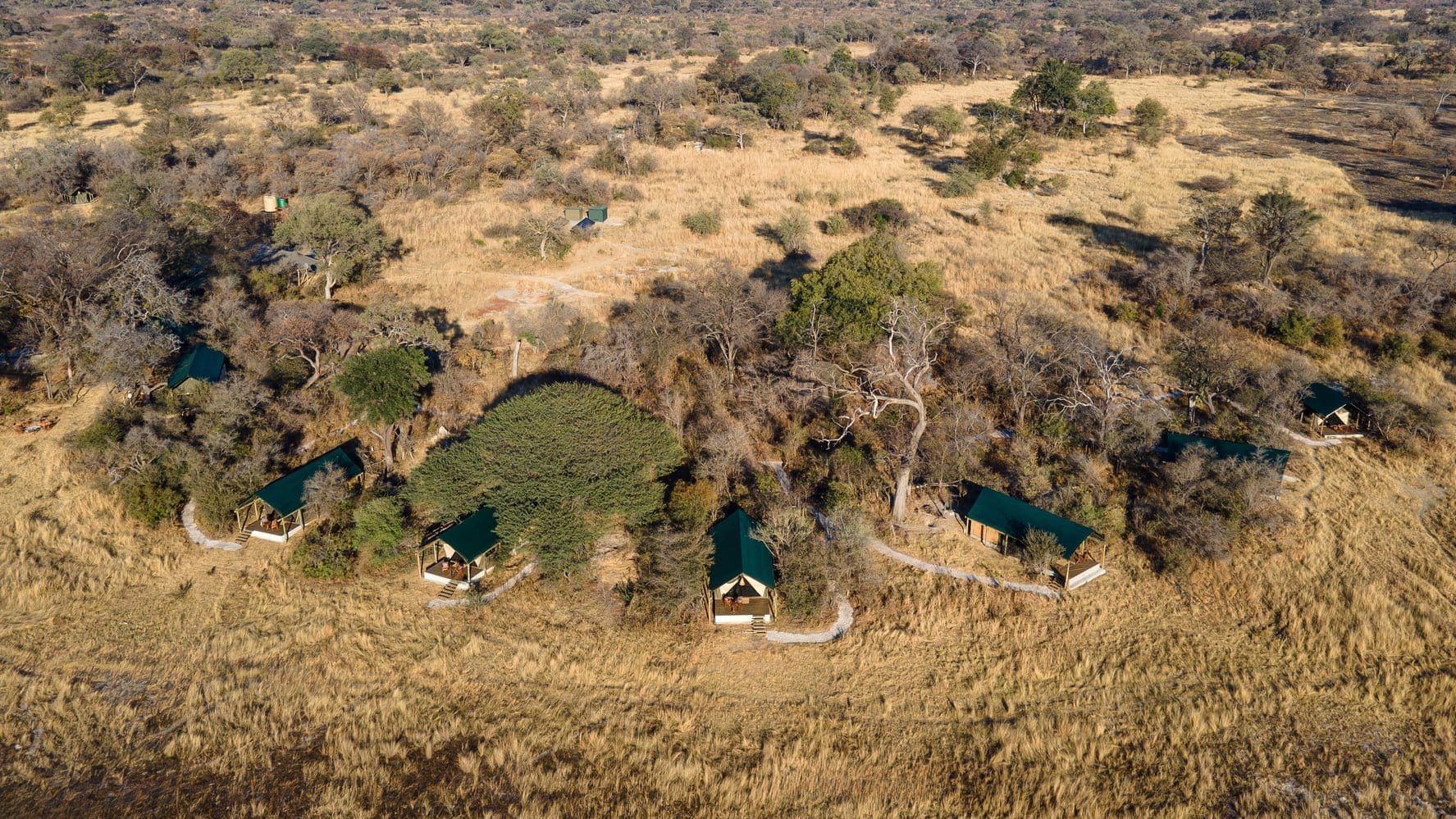 Luftaufnahme des Luiana Plains Safaris Camps mit mehreren Zeltunterkünften inmitten von Savanne und Bäumen.