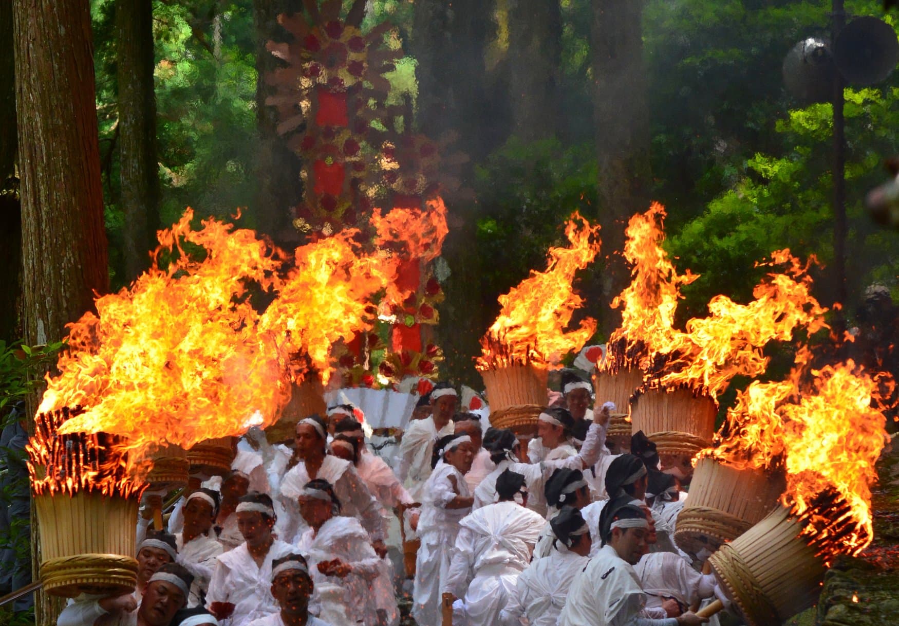 Menschen in weißer Kleidung tragen große brennende Fackeln beim Nachi-no-Ogi-Feuerfest im Kumano Nachi Taisha durch den Wald.