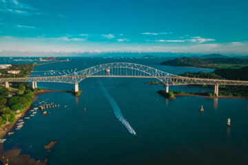 Vogelperspektive auf die Brücke der Amerikas über den Panamakanal. Unter der Brücke fährt gerade ein Schlepper entlang