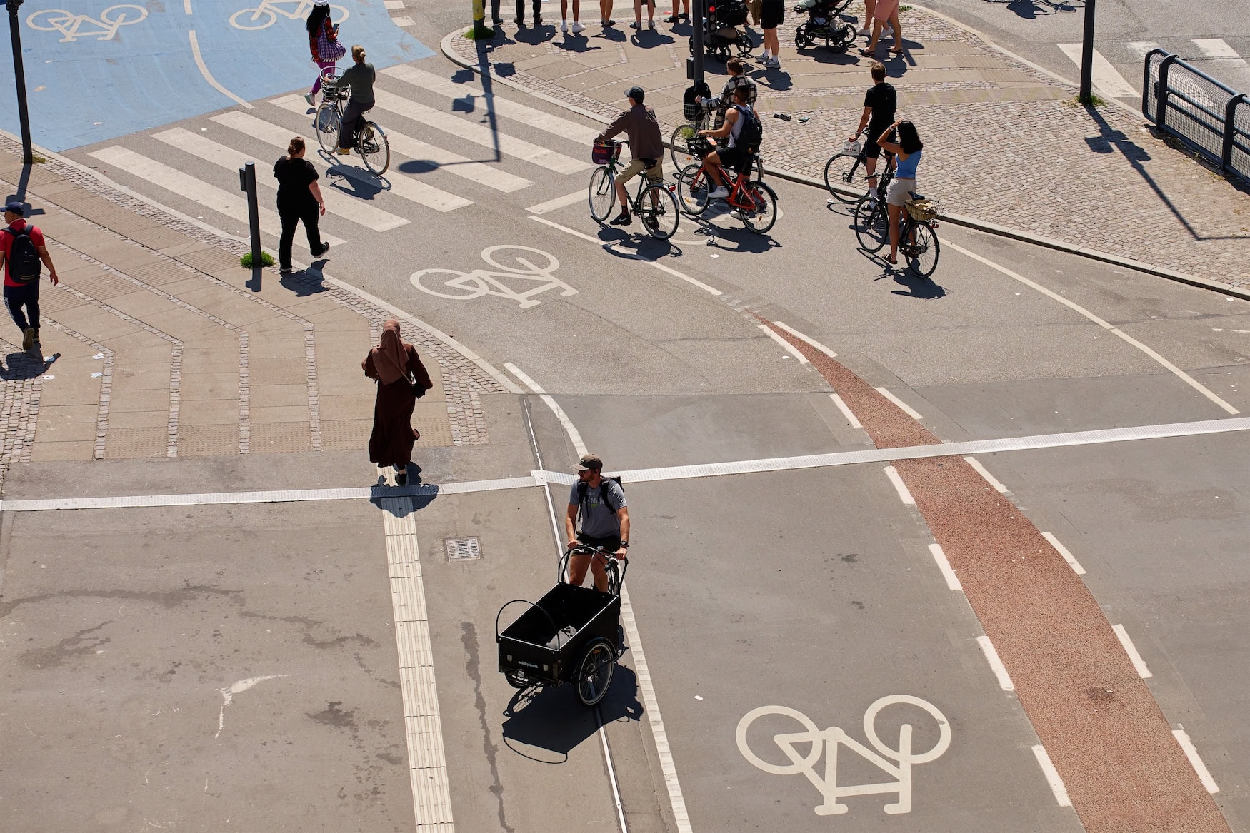 Von oben fotografierte Kreuzung mit Radwegen, Fahrradsymbolen und Fußgängerüberweg im Sommer
