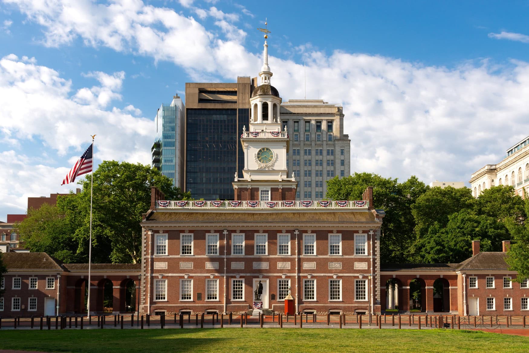 Panoramaaufnahme der Independence Hall in Philadelphia, davor ein Rasen, dahinter einige Hochhäuser.