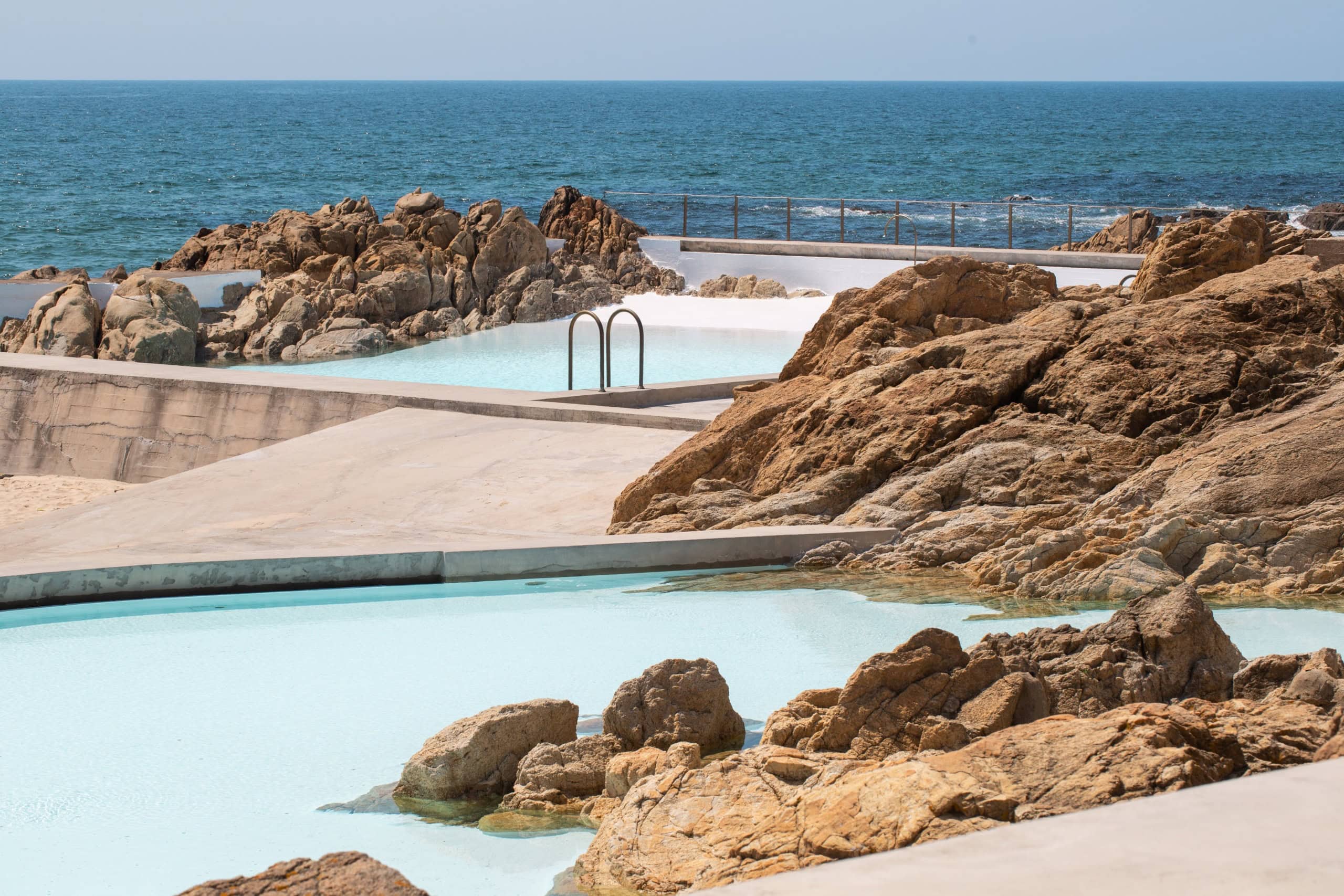 Meerwasserbecken der Piscina das Marés in Portugal mit Blick auf den Atlantik, umgeben von hellen Betonflächen und dunklen Felsen.