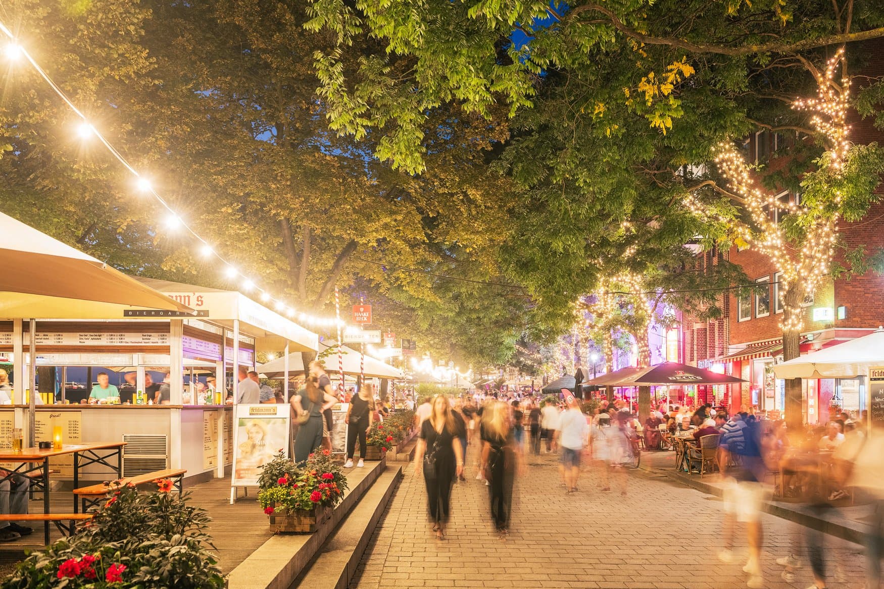 Abends beleuchtete Schlachte in Bremen mit Lichterketten in den Bäumen, Biergartenständen und Passanten auf der Promenade.