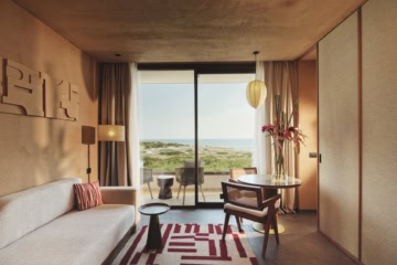 Wohnbereich einer Suite mit Sofa, rundem Tisch und Balkon mit Meerblick im Icona's Costa Ragusa Resort.