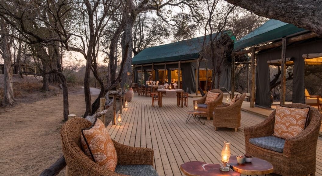 Überdachte Terrasse mit Sitzgruppe und Blick auf das Gästezelt im Luiana Plains Safaris Camp.