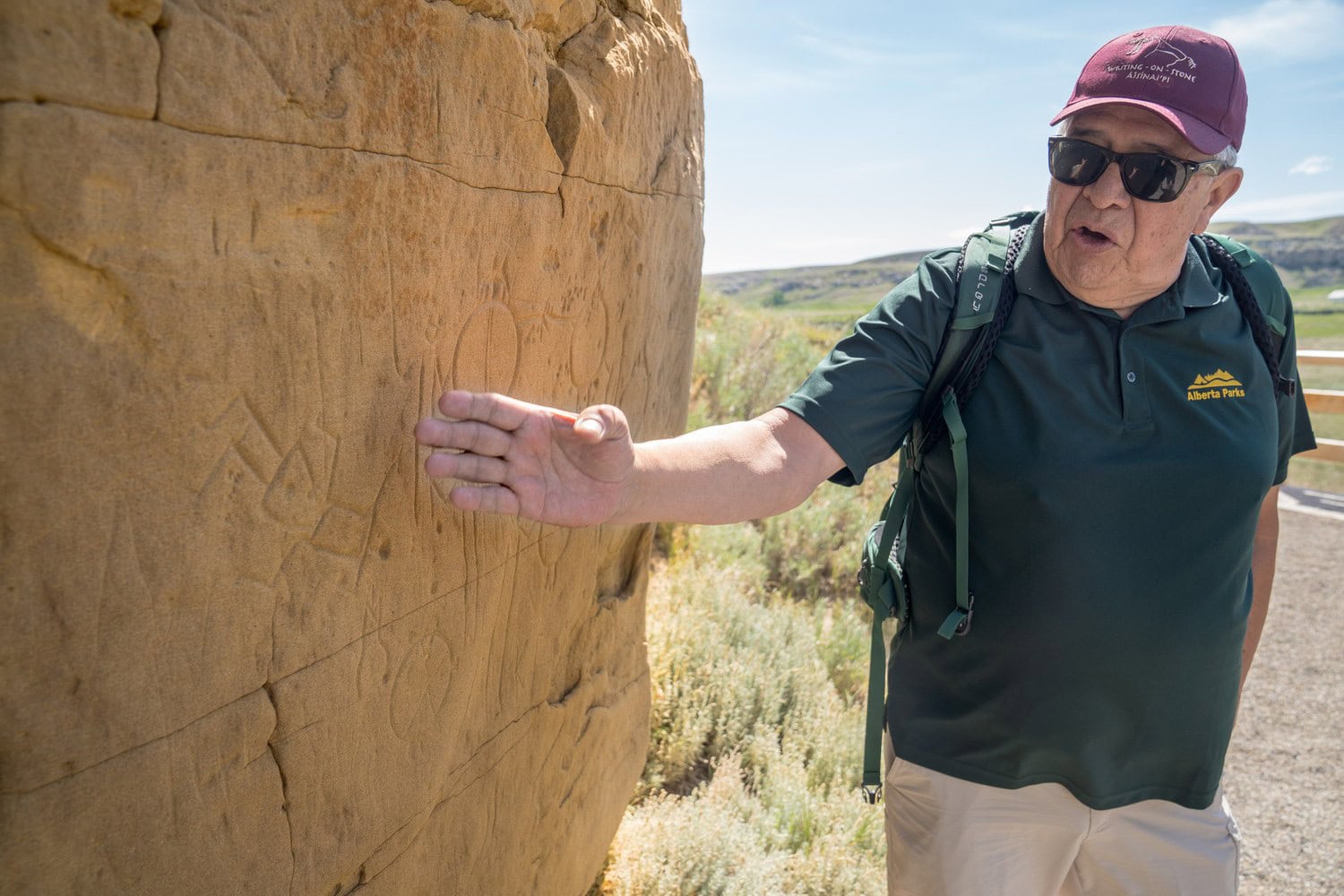 Guide von Alberta Parks zeigt Besuchern eingeritzte Figuren auf einer Sandsteinwand im Writing-on-Stone Provincial Park bei Milk River